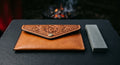 Hand tooled leather sharpening stone pouch with a carved rose flap beside a grey bench stone