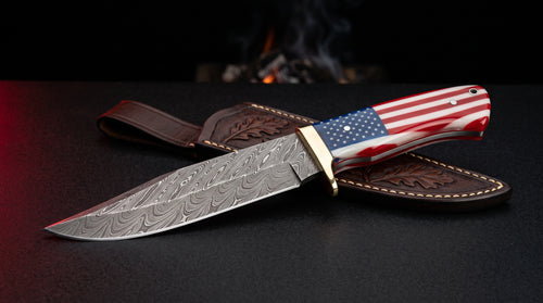 Damascus Bowie knife with brass guard and full resin American flag handle beside a leather sheath