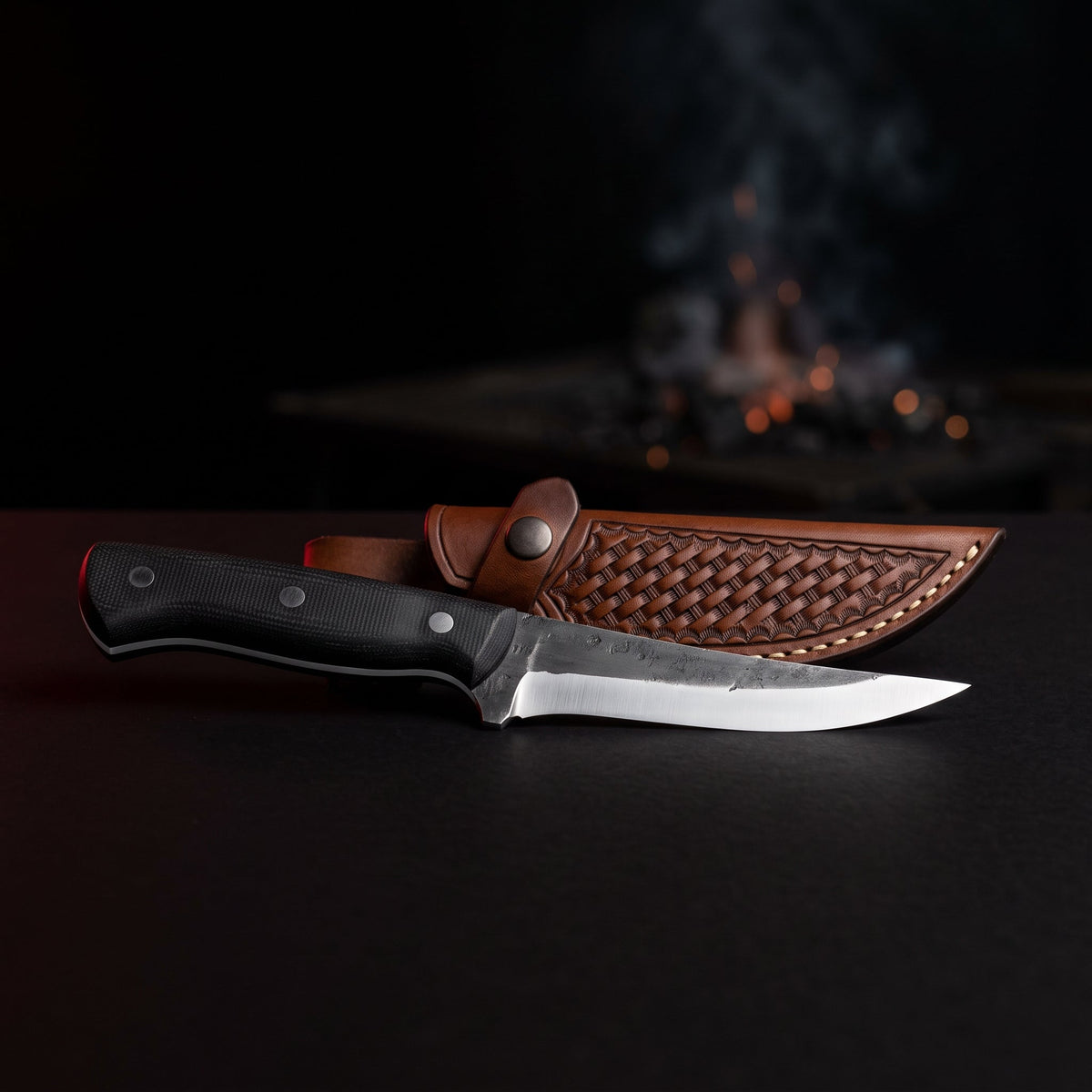 Hand forged boning knife with a 5 inch straight carbon steel blade, black micarta handle and a stamped leather sheath