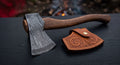 Damascus bushcraft axe with a ladder pattern head, curved walnut handle and a hand carved leather head cover
