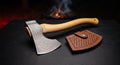 Damascus bushcraft axe with a raindrop pattern head, curved hickory handle and a stamped leather head cover