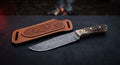 Damascus cowboy knife with a twist pattern drop point blade, stag antler handle and a hand carved pancake sheath