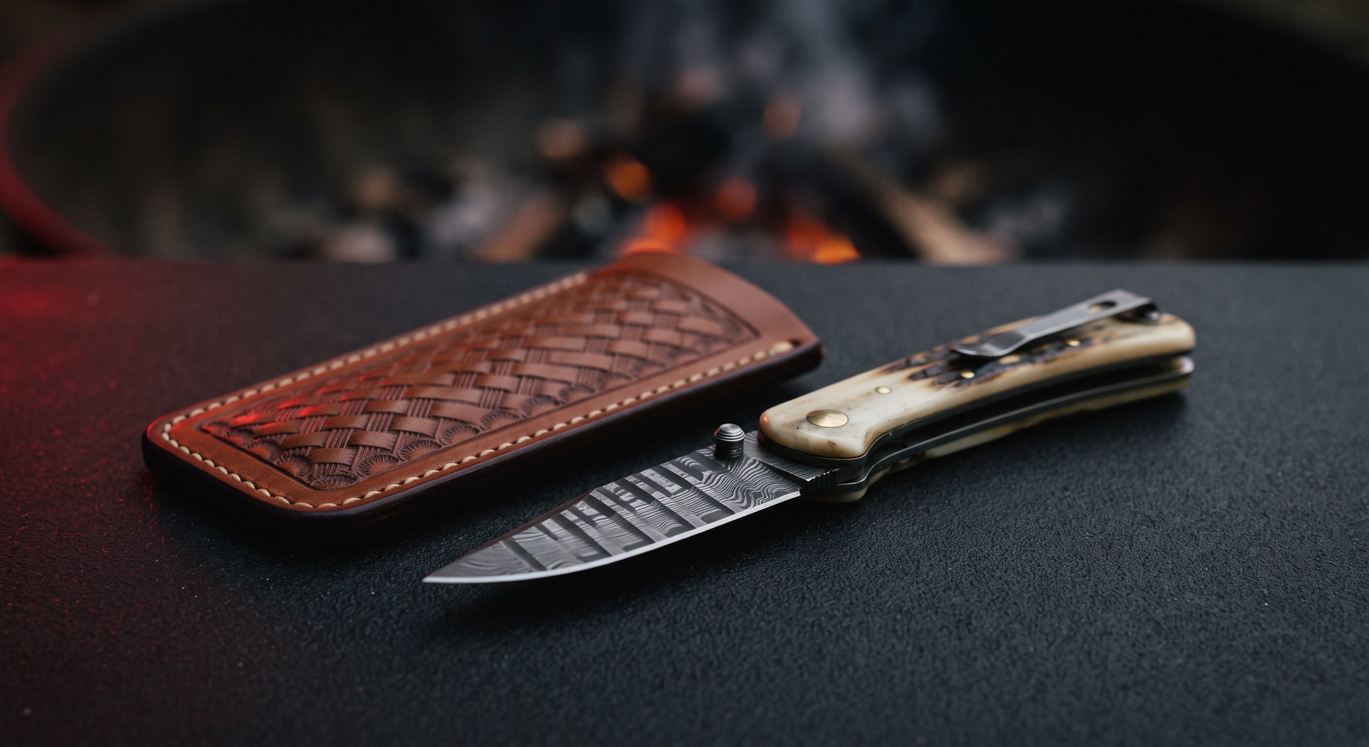 Closed Damascus liner lock folding knife with a camel bone handle, thumb stud and a leather slip pouch