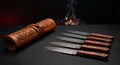 Damascus steak knife set of five with rosewood handles beside a closed hand carved leather knife roll