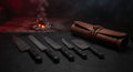 Damascus BBQ knife set of five with black handles beside a closed tooled leather knife roll