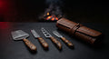 Damascus cheese knife set of four with burl wood handles beside a closed tooled leather knife roll
