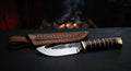 Hand forged gut hook skinner with a notch cut into the spine and a stacked leather handle with brass fittings