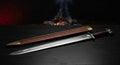 Hand forged viking sword with a broad fullered blade, iron lobed pommel and a stamped leather scabbard