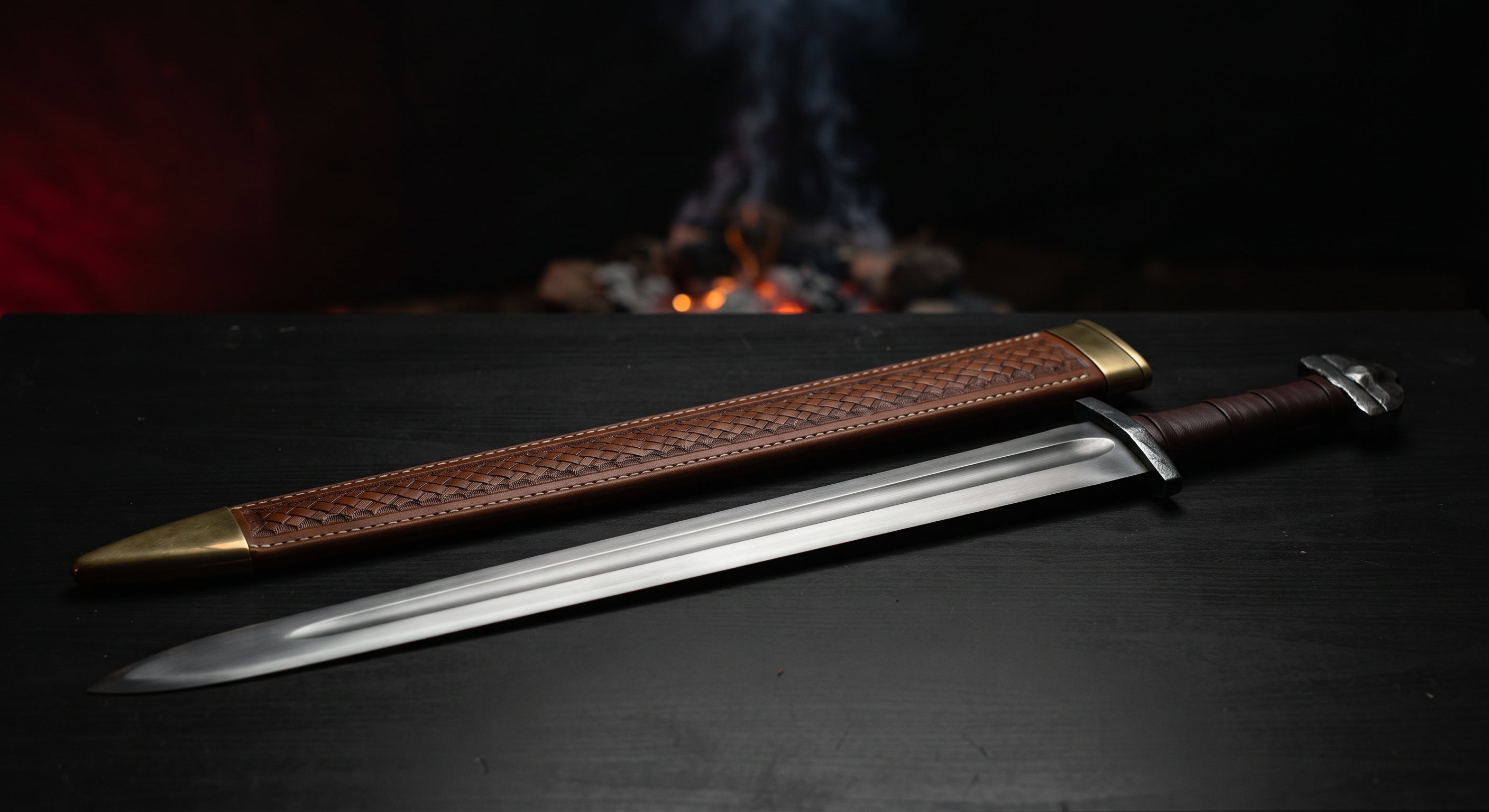Hand forged viking sword with a broad fullered blade, iron lobed pommel and a stamped leather scabbard
