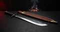 Hand forged falchion with a single edged blade widening toward the tip, iron disc pommel and a stamped leather scabbard